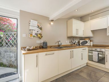 A kitchen with cream cabinets wooden countertops a sink an oven a microwave and a glass door leading outside at 2 Bryn Tirion in Llan Ffestiniog