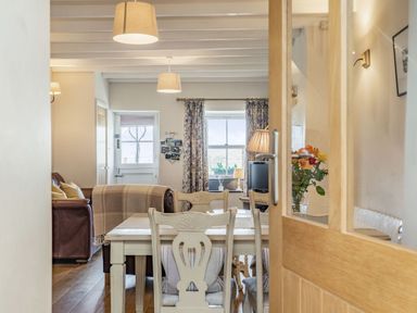 A dining area with wooden table and chairs next to a living room with a leather sofa and a window at 2 Bryn Tirion in Llan Ffestiniog