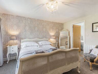 A bedroom with a bed a patterned wallpaper two bedside tables with lamps a standing mirror an armchair and an open door at 2 Bryn Tirion in Llan Ffestiniog