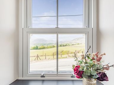 A window with a view of a rural landscape with fields and mountains and flowers on a windowsill at 2 Bryn Tirion in Llan Ffestiniog