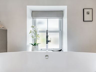 A bathroom with a bathtub under a window with a flowerpot and a framed picture on the wall at 2 Bryn Tirion in Llan Ffestiniog