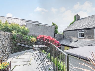 An outdoor patio area with a small table and chairs surrounded by stone walls and flowering plants at 2 Bryn Tirion in Llan Ffestiniog