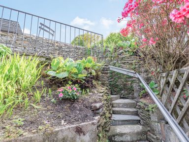 An outdoor stone stairway with plants and a metal railing leading up to a patio with metal chairs and table at 2 Bryn Tirion in Llan Ffestiniog
