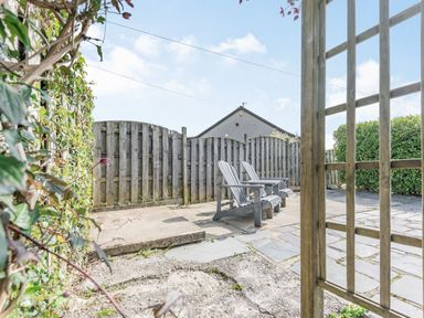 A patio area with two wooden chairs a wooden fence and a bush at 2 Bryn Tirion in Llan Ffestiniog