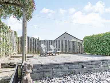 A patio area with two wooden chairs against a wooden fence and a stone statue in the foreground at 2 Bryn Tirion in Llan Ffestiniog