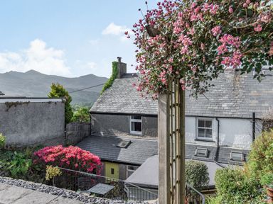 A backyard with flowering plants a wooden trellis and a gray roof house with mountain views at 2 Bryn Tirion in Llan Ffestiniog