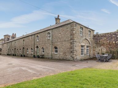 A stone building with multiple windows and outdoor chairs and table on the side at Reiver's Rest in Hesleyside near Bellingham