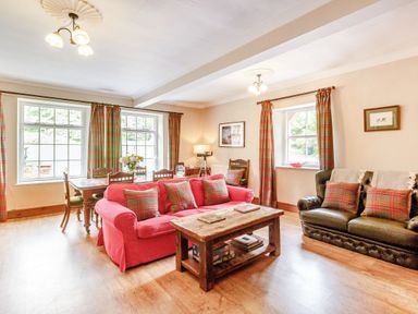 A living room with a red sofa and a wooden coffee table next to a black sofa with plaid cushions at Reiver's Rest in Hesleyside near Bellingham