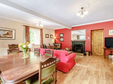 A living room with a wooden dining table and chairs red sofas a fireplace and a television at Reiver's Rest in Hesleyside near Bellingham