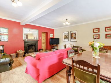A living room with red walls a fireplace a red sofa wooden dining table and flower vase at Reiver's Rest in Hesleyside near Bellingham