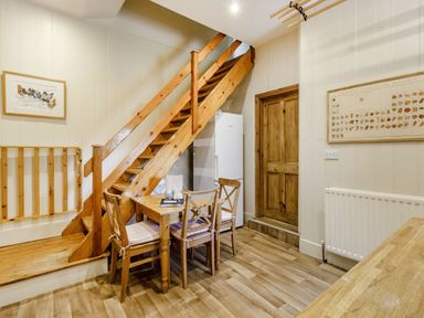 A dining area with a wooden table and four chairs under wooden stairs near a refrigerator and a wooden door at Reiver's Rest in Hesleyside near Bellingham