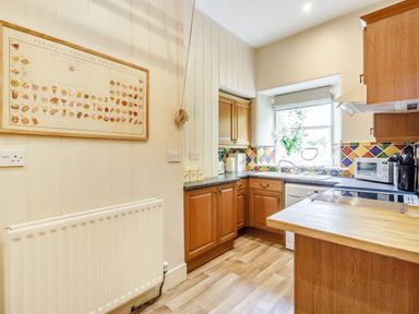A kitchen with wooden cabinets a window a countertop with appliances and a framed periodic table of desserts on the wall at Reiver's Rest in Hesleyside near Bellingham