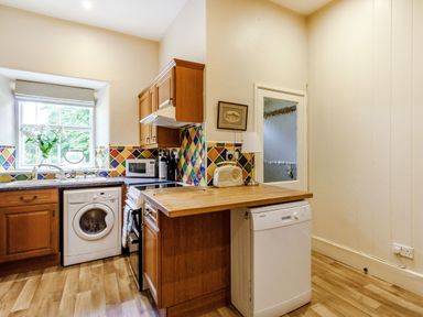 A kitchen with wooden cabinets washing machine dishwasher and a window with flowers at Reiver's Rest in Hesleyside near Bellingham