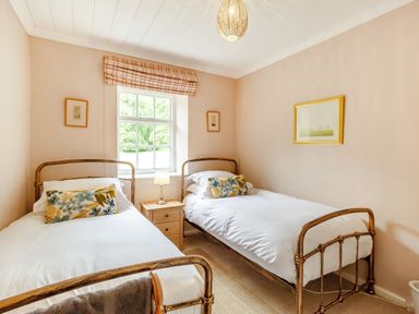 A bedroom with two single beds a wooden nightstand between them and a window with a plaid Roman shade at Reiver's Rest in Hesleyside near Bellingham