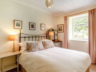 A bedroom with a bed with floral pillows bedside tables lamps framed pictures and a window with checked curtains at Reiver's Rest Hesleyside near Bellingham