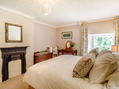 A bedroom with a bed pillows a window and furniture including a fireplace at Reiver's Rest in Hesleyside near Bellingham