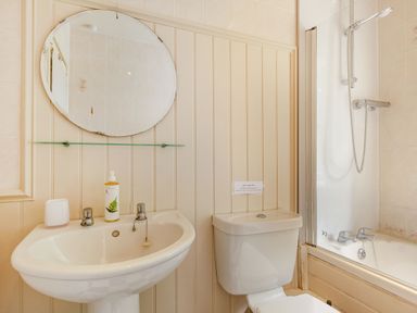 A bathroom with a sink a round mirror a toilet and a bathtub with a shower at Reiver's Rest in Hesleyside near Bellingham