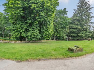 A grass lawn with trees a stone wall and a wooden bench at Reiver's Rest in Hesleyside near Bellingham