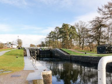 A canal lock with grassy banks and trees near a pathway at Glen Dessary in Corpach near Fort William