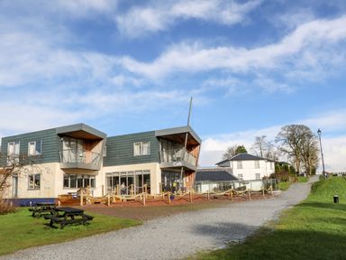 A modern two story building with balconies and a cafe sign next to a gravel path and picnic tables at Glen Dessary Corpach near Fort William