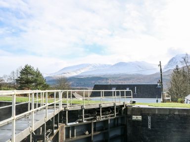 A canal lock with metal gate and railing in front of a house with snow-covered mountains in the background at Glen Dessary in Corpach near Fort William