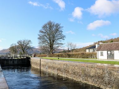 A water canal with stone walls and leafless trees near white buildings at Glen Dessary in Corpach near Fort William
