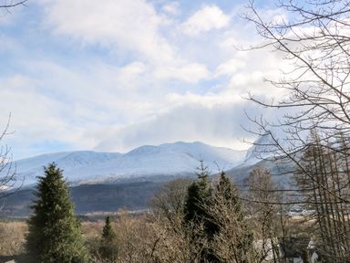 A snowy mountain range in the background with trees and houses in the foreground at Glen Dessary in Corpach near Fort William