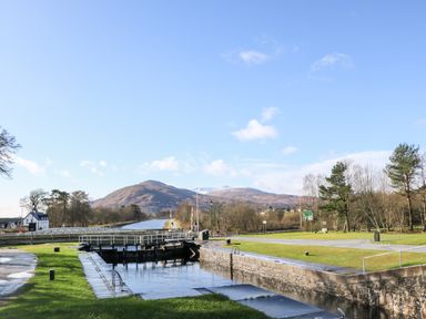 A canal lock with gates surrounded by grassy areas and trees with hills in the background at Glen Dessary in Corpach near Fort William
