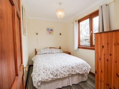 A bedroom with a double bed a wooden wardrobe striped carpet and a window with curtains at Glen Dessary in Corpach near Fort William