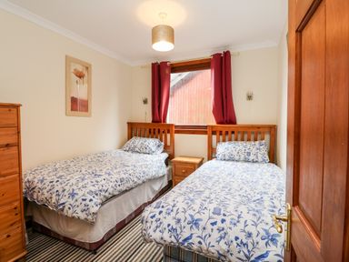 A bedroom with two single beds and floral bedding a wooden dresser and window with red curtains at Glen Dessary in Corpach near Fort William