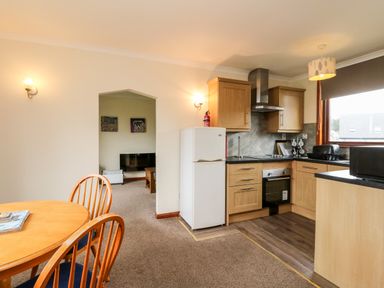 A kitchen with wooden cabinets a white refrigerator and a dining table with chairs at Glen Dessary in Corpach near Fort William