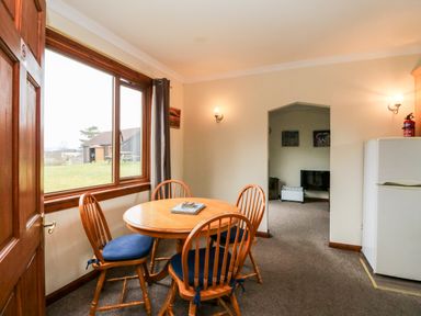A dining area with a round wooden table and four chairs next to a window and a white refrigerator at Glen Dessary in Corpach near Fort William