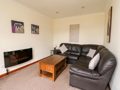 A living room with a brown leather sectional sofa wooden coffee table and wall-mounted electric fireplace at Glen Dessary in Corpach near Fort William