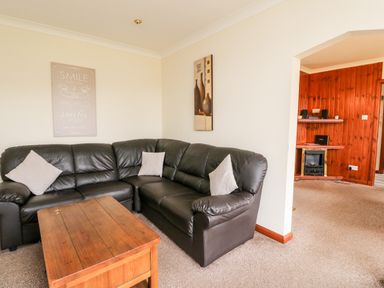 A living room with a brown leather corner sofa a wooden coffee table and wall art at Glen Dessary in Corpach near Fort William