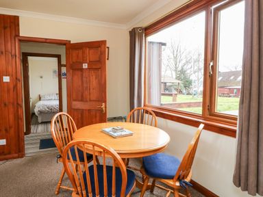 A dining area with a round wooden table and four chairs with blue cushions next to a large window showing an outdoor view at Glen Dessary in Corpach near Fort William