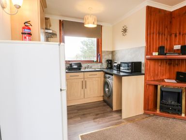 A kitchen area with a refrigerator fire extinguisher washing machine toaster microwave coffee maker and a wooden fireplace at Glen Dessary in Corpach near Fort William