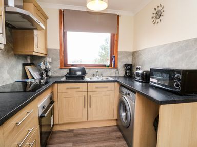 A kitchen with wooden cabinets a washing machine a microwave a toaster and a window at Glen Dessary in Corpach near Fort William