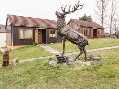 A large deer statue on grass in front of two wooden houses at Glen Dessary Corpach near Fort William