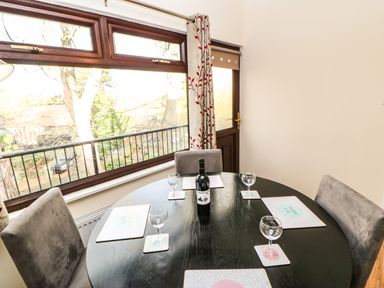 A dining area with a round black table four chairs placemats wine glasses and a bottle of wine next to a window and door at Primrose Lodge in Saltburn-by-the-Sea