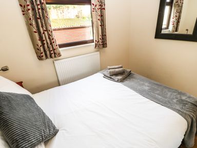 A bedroom with a double bed a gray pillow folded towels on the bed curtains with leaf patterns and a mirror on the wall at Primrose Lodge in Saltburn-by-the-Sea