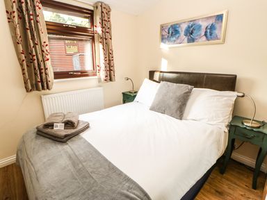 A bedroom with a double bed pillows and towels on the bed bedside tables with lamps a window with curtains and a painting on the wall at Primrose Lodge in Saltburn-by-the-Sea
