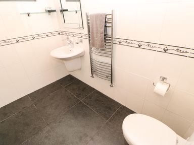 A bathroom with a wall-mounted sink a heated towel rail with a towel toilet with a toilet paper holder and tiled walls and floor at Primrose Lodge in Saltburn-by-the-Sea