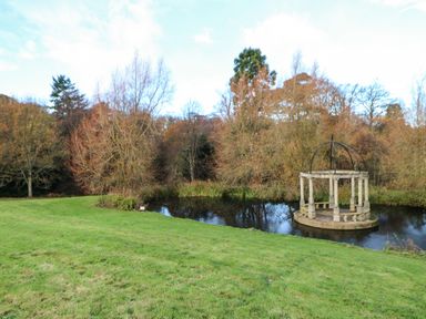 A grassy area with a small pond and a stone gazebo surrounded by trees in Primrose Lodge Saltburn-by-the-Sea