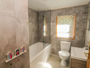 A bathroom with a bathtub shower toilet and sink with fish patterned window blind at Striding Edge White Cross Bay near Troutbeck Bridge