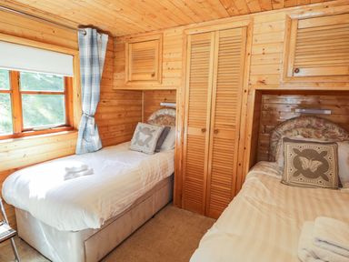 A bedroom with two single beds between wooden wardrobes and a window with curtains at Striding Edge White Cross Bay near Troutbeck Bridge