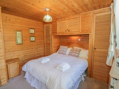A bedroom with a double bed white bedding wooden walls wooden cabinets and framed flower pictures at Striding Edge in White Cross Bay near Troutbeck Bridge