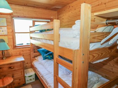 A wooden bunk bed with white bedding a wooden dresser with a lamp and a window in a wooden paneled room at Striding Edge White Cross Bay near Troutbeck Bridge