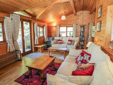 A wooden living room with two beige sofas red and floral cushions wooden tables and floral curtains at Striding Edge in White Cross Bay near Troutbeck Bridge
