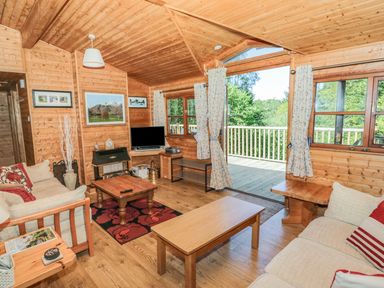A wooden living room with sofas coffee tables a television and an open door leading to a deck at Striding Edge White Cross Bay near Troutbeck Bridge