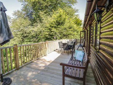 A wooden deck with a bench and dining table next to a log cabin at Striding Edge White Cross Bay near Troutbeck Bridge